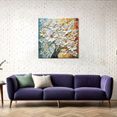 A framed abstract artwork featuring a tree with white flowers, displayed above a purple couch with a green pillow, in a room with white brick wall and a wooden floor.