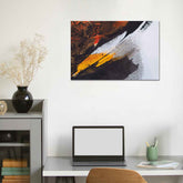 A canvas print featuring an abstract painting with black, white, and yellow hues, displayed above a desk with a laptop and a vase with dried flowers.