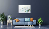 A framed canvas print featuring a vibrant floral composition, displayed on a wall above a blue sofa with orange and white throw pillows, accompanied by a wooden side table hosting a white vase with a green plant.
