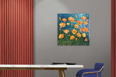A canvas print featuring a painting of orange flowers in the grass, displayed on a wall above a modern desk and chair.