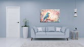 A canvas painting of a bird on a branch with floral elements, displayed above a grey sofa in a room with a light blue wall.