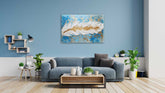 A framed canvas print featuring a leaf and feather pattern, displayed on a wall above a blue sofa in a living room setting with wooden flooring and decorative plants.