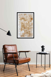 A geometric square shape canvas print hanging on a wall over a white chair and wooden floor, with a framed picture to the side and a lamp above the chair.