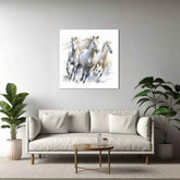 A canvas painting of white horses running, displayed above a beige sofa in a room with decorative plants.