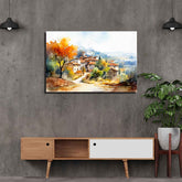 A canvas print depicting a landscape with a village and autumn trees, displayed on a gray wall in a modern interior setting.