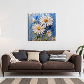 A painting of white flowers with a blue background, hung on a wall above a brown sofa with various pillows, in a room with striped flooring.