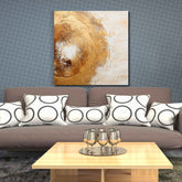 A canvas print featuring an abstract colorful painting displayed above a sofa with patterned pillows, placed in a room with grey walls and a wooden floor.