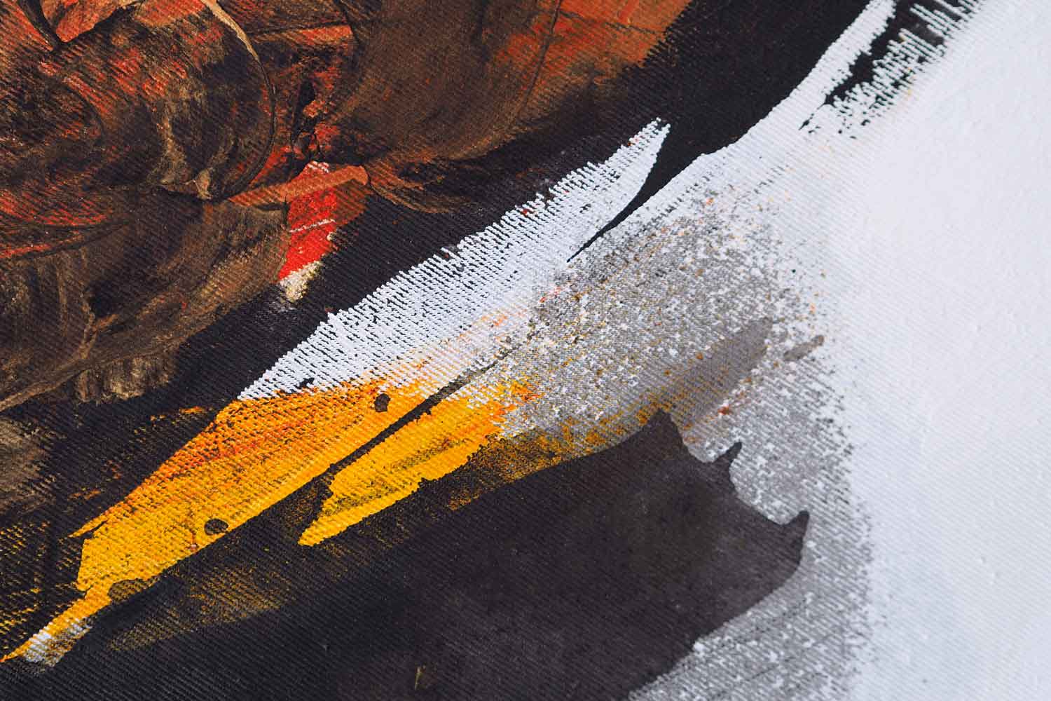 A canvas print featuring an abstract painting with black, white, and yellow hues, displayed above a desk with a laptop and a vase with dried flowers.