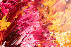 A canvas oil painting displayed above a pink sofa in a room with a light interior, featuring abstract red and yellow colors.