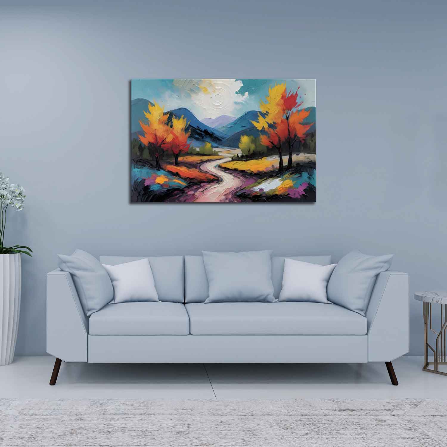A canvas print featuring a vibrant painting with a winding road, trees, and a mountain range in the background, displayed above a gray sofa in a room with a light blue wall.