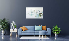 A framed canvas print featuring a vibrant floral composition, displayed on a wall above a blue sofa with orange and white throw pillows, accompanied by a wooden side table hosting a white vase with a green plant.