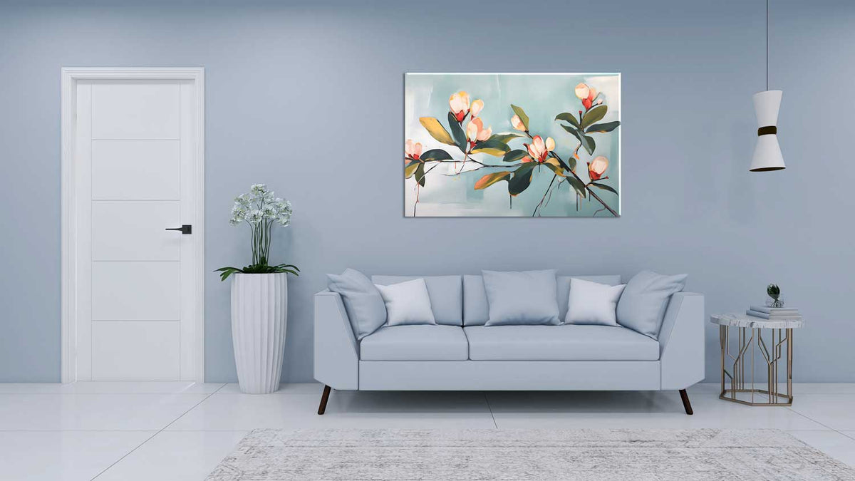 A canvas print of magnolia branches hanging on a wall above a grey sofa, with a white door and a potted plant in the background.