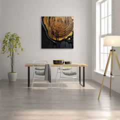A canvas print featuring an abstract wooden figure displayed on a wall above a dining table and chairs in a room with a wooden floor and a window.