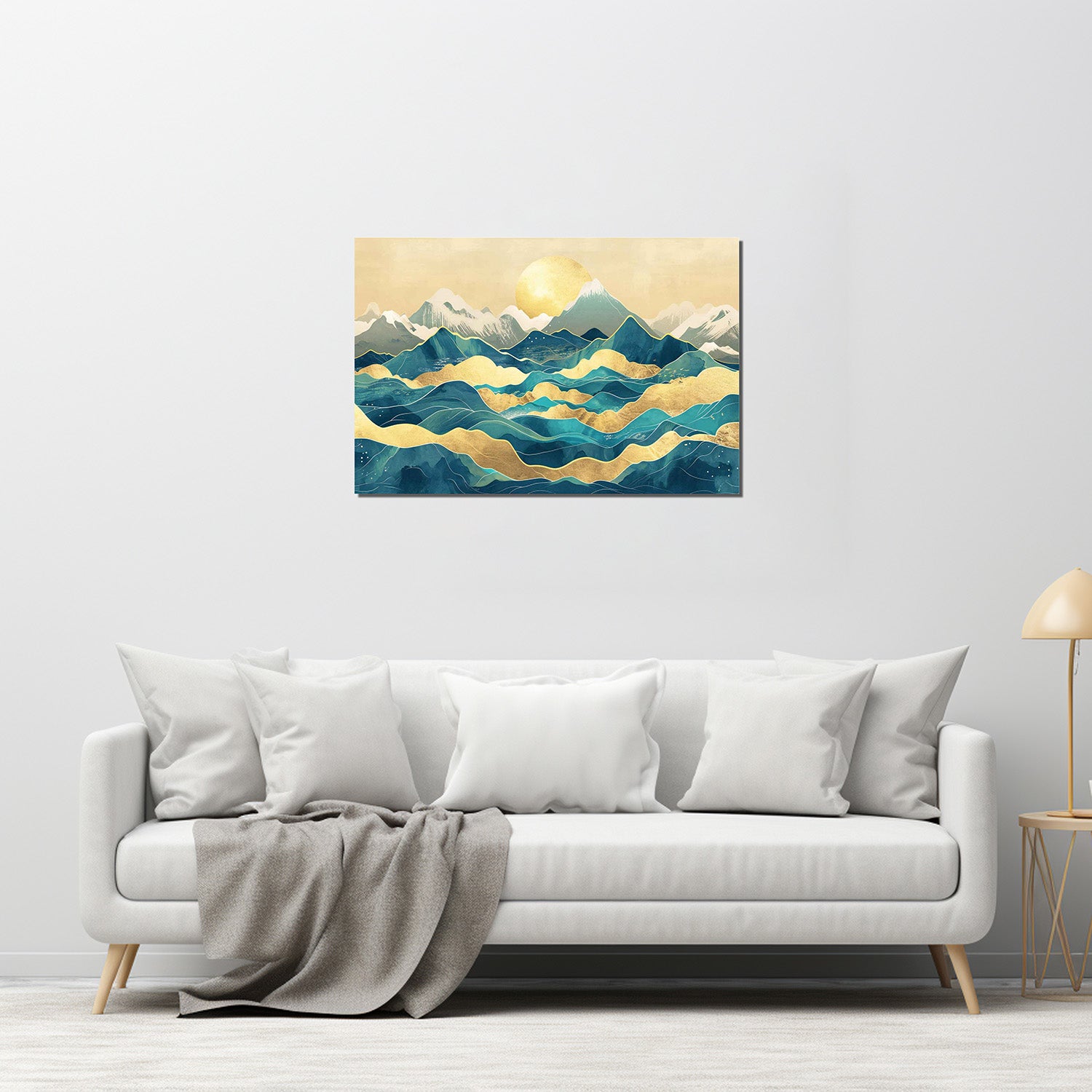 A canvas print featuring a mountainous landscape with a golden line in the sky, displayed on a wall above a white sofa with grey pillows.