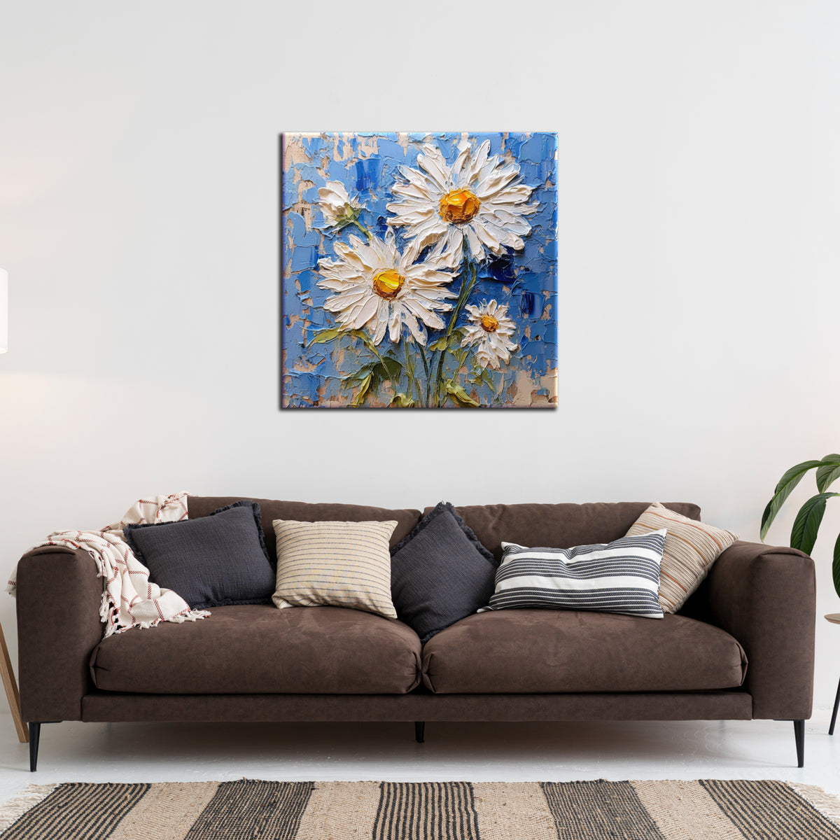 A painting of white flowers with a blue background, hung on a wall above a brown sofa with various pillows, in a room with striped flooring.